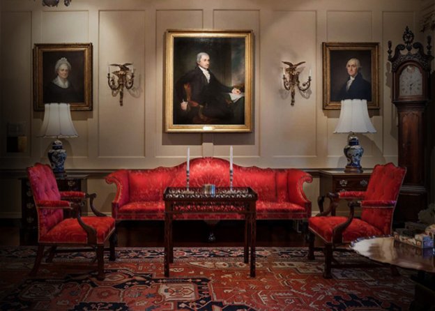 Historic room furnished with period furniture, portraits, and grandfather clock